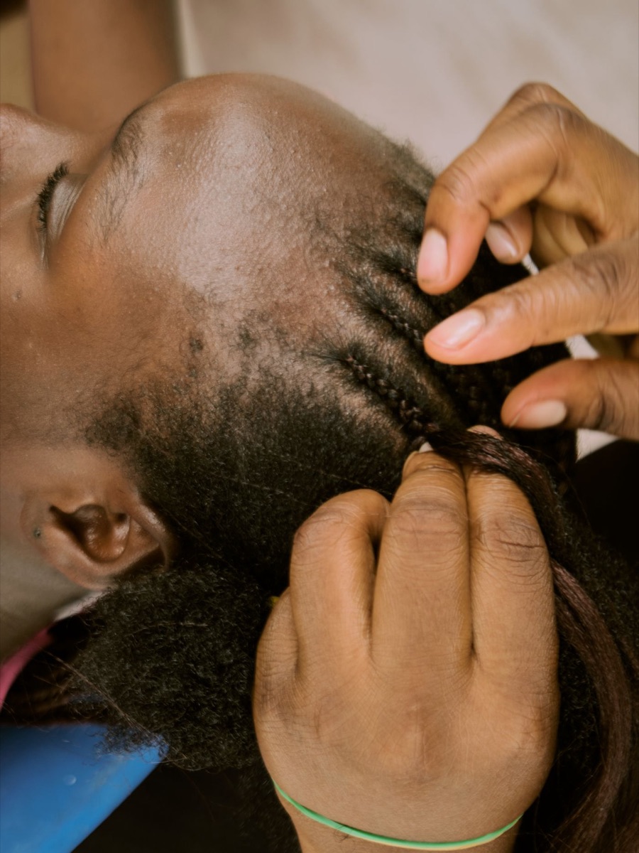 Braider parting and braiding a client's hair close to the scalp